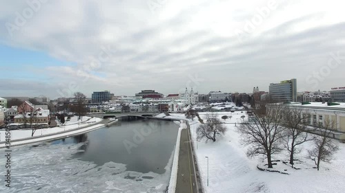 smooth take-off over the river, which is located in the city, flight over the demolished city in winter, houses, roofs in the snow, roads with cars and trees without leaves are visible, the river has  photo
