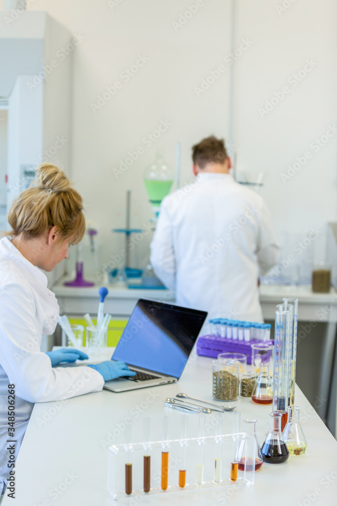 Chemist with rubber gloves working on laptop in laboratory Chemist with rubber gloves working on laptop in laboratory