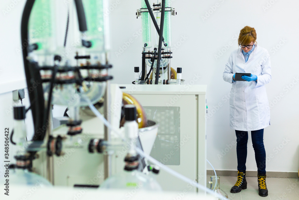 Chemist working on tablet next to rotavapor machine in laboratory Chemist working on tablet next to rotavapor machine in laboratory