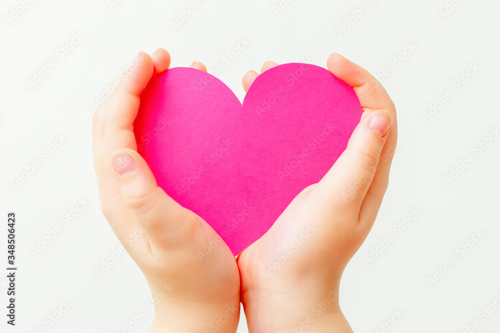 Closeup of paper heart in little hands of child on white background. Pink heart in hands on white.