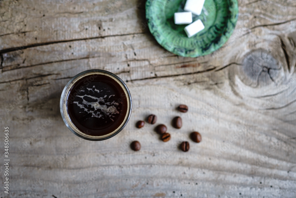 Kaffee in einem Glas und ein Teller mit Würfelzucker auf einem grauen Holztisch. Rustikaler Stil, Espresso, Draufsicht. Kaffee in einem Glas und ein Teller mit Würfelzucker auf einem grauen Holztisch. Rustikaler Stil, Espresso, Draufsicht.