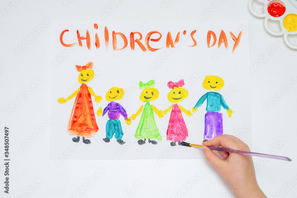 Top view of hand of child drawing the colorful children with brush by watercolors with words Children's Day on a white paper. Top view of hand of child drawing the colorful children with brush by watercolors with words Children's Day on a white paper.