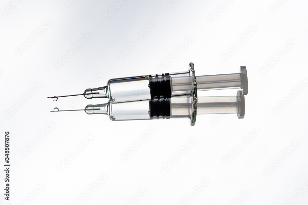 Glass syringe with reflection on white background. Concept about vaccine of coronavirus or COVID-19. Glass syringe with reflection on white background. Concept about vaccine of coronavirus or COVID-19.