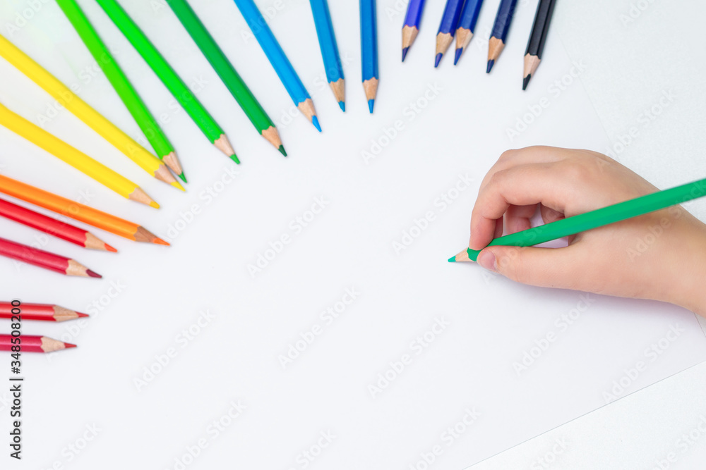 Top view of child's hand on empty white sheet of paper with set of colored pencils. Copy space for text. Top view of child's hand on empty white sheet of paper with set of colored pencils. Copy space for text.