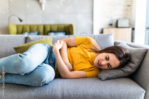 Tableau sur toile Sick woman lying on sofa in the living room with stomach ache