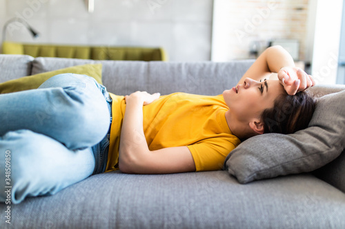 Young woman with stomach ache lying on a sofa
