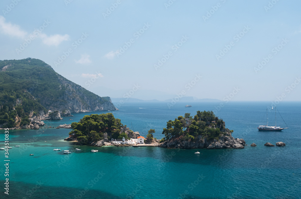 in the bay of Parga, an island and a chapel, boats are waiting on the blue Mediterranean sea,