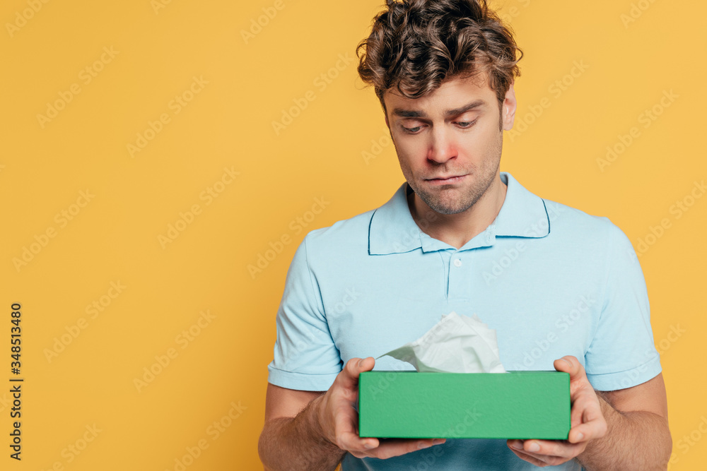 Sad and sick man holding box with napkins isolated on yellow Sad and sick man holding box with napkins isolated on yellow