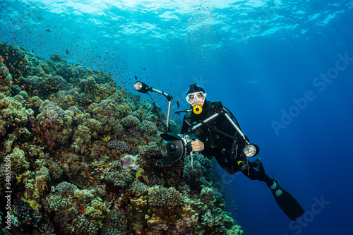 typical Red Sea tropical reef with hard and soft coral surrounded by school of orange anthias and a underwater photographer diver