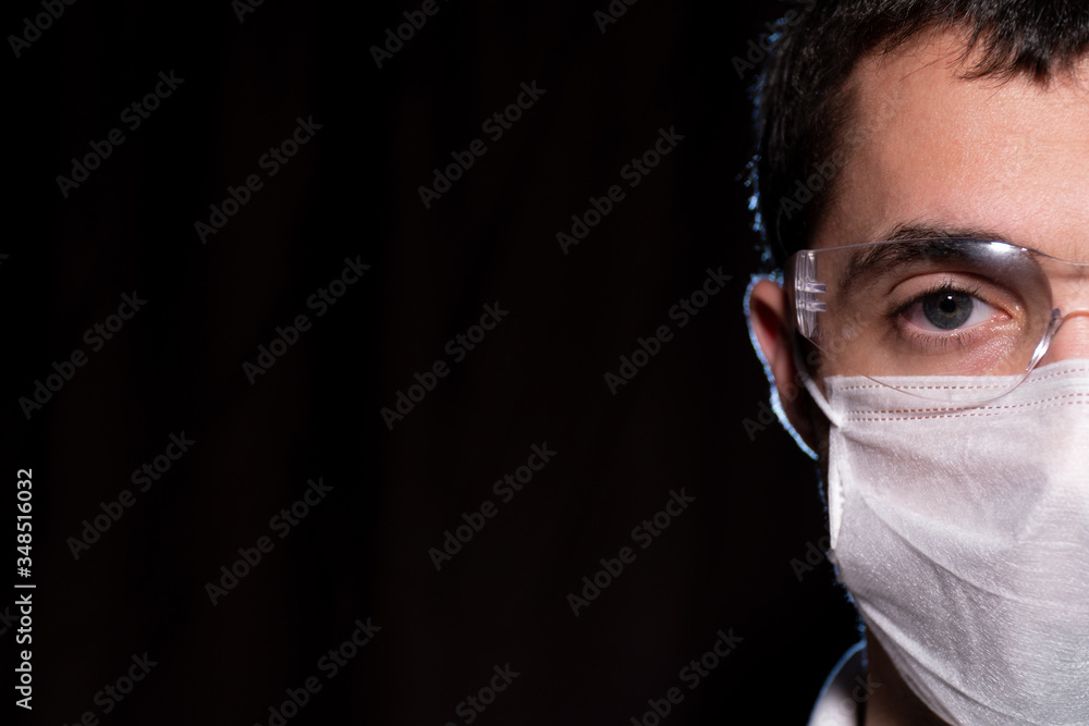 Concept photo half face of a young man wearing mask and goggles on black background. Young doctor in medical mask and goggles. Protective mask and goggles on handsome man Concept photo half face of a young man wearing mask and goggles on black background. Young doctor in medical mask and goggles. Protective mask and goggles on handsome man