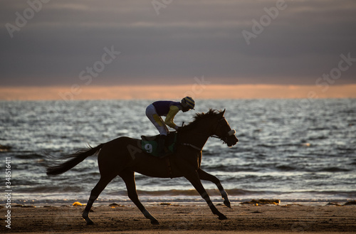Silhouette of race horse and jockey racing on the beach at sunset, wild Atlantic way on the west coast of Ireland