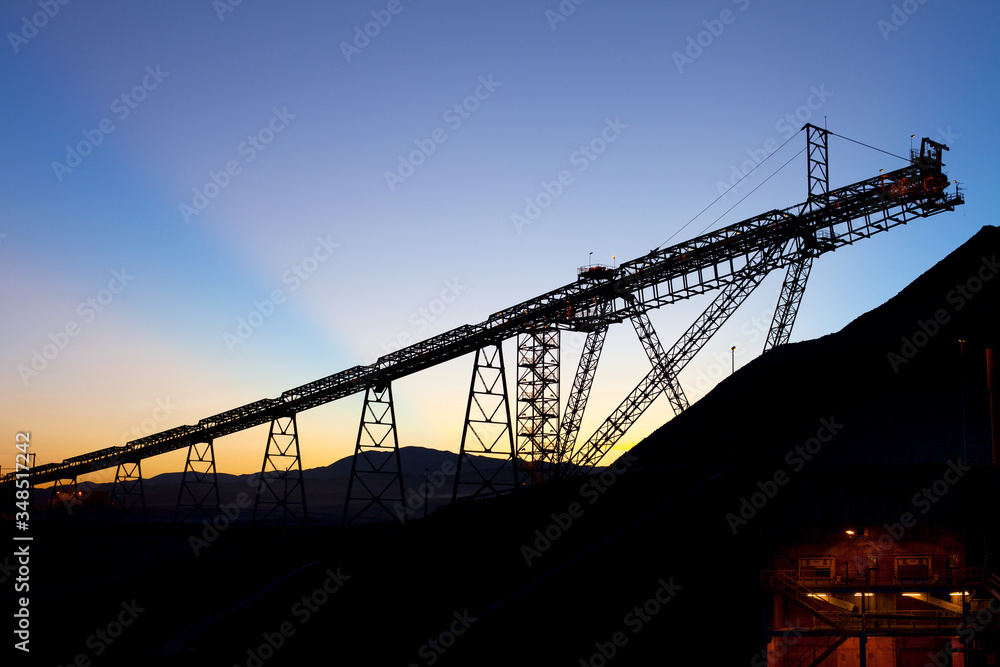 Fototapeta premium Sunrise behind silhouetted stockpile and conveyor belt in a copper mine at the Atacama Desert, Chile