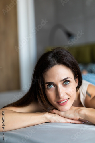 Happy pensive young woman lying and thinking on bed. Thoughtful beautiful girl lying on bed while looking up.