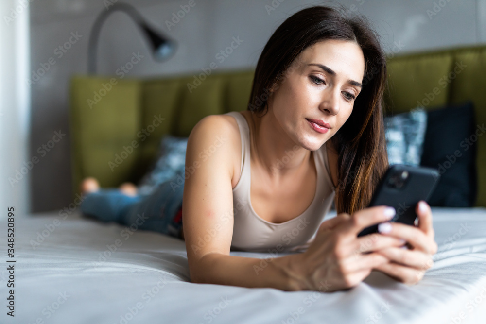 Young beautiful girl looking at a mobile phone while lying in bed Young beautiful girl looking at a mobile phone while lying in bed