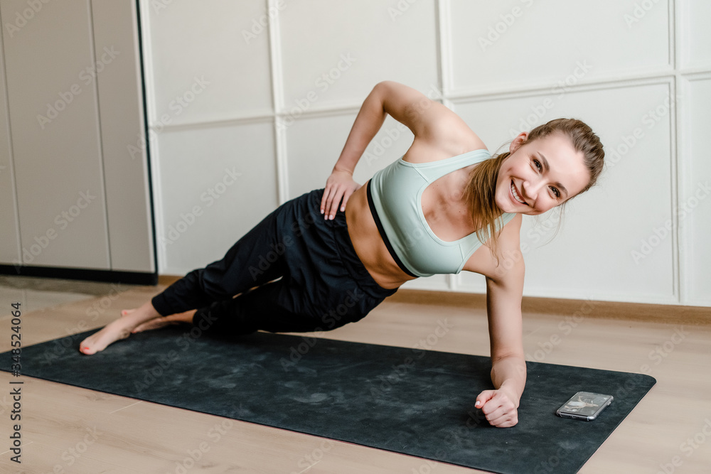 beautiful smiling woman doing sport exercise with phone on yoga mat at home