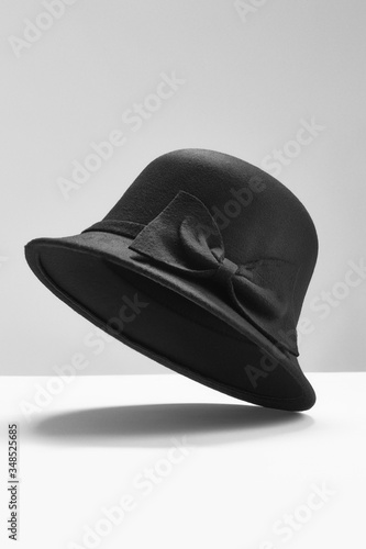 Subject shot of a black cloche hat decorated with a wide black band and a bow. The stylish hat is raised off the white surface against the gray backdrop. photo