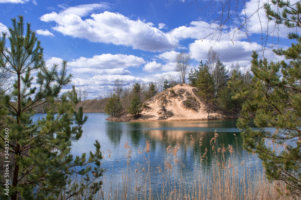 Picturesque landscape of the lake with blue water, sky with white clouds and coniferous woodlands on the steep banks.