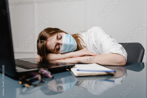 woman at home office with laptop wearing mask and sleeping tired
