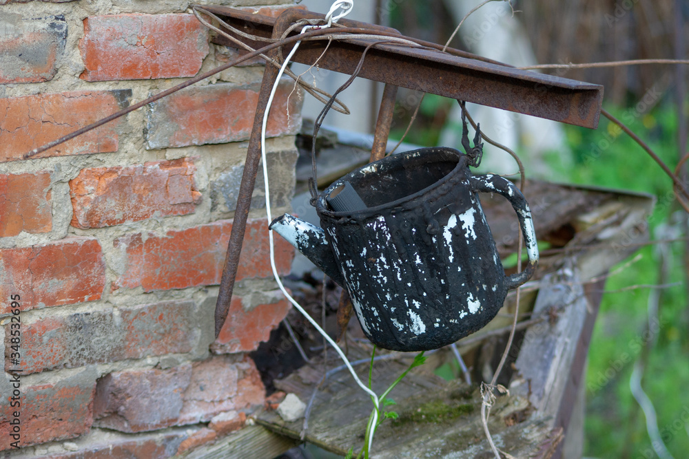 An old teapot smeared with black tar. Against a brick wall and rusty scrap metal.