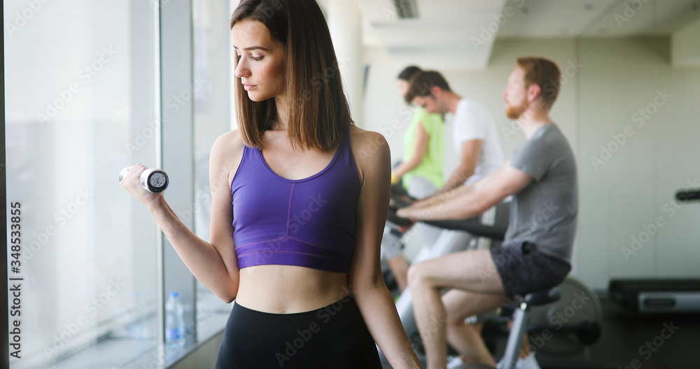 Young beautiful woman doing exercises with dumbbell in gym