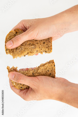 Hands tearing slice of cereal bread on two pieces. Delicious rye loaf and pastry for sandwich isolated on white background. Studio shot. Top view. Homemade bakery and nutrition concept
