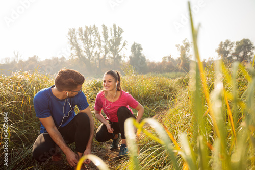 Happy young Caucasian couple preparing for early morning jogging exercise, tying shoelaces and talking