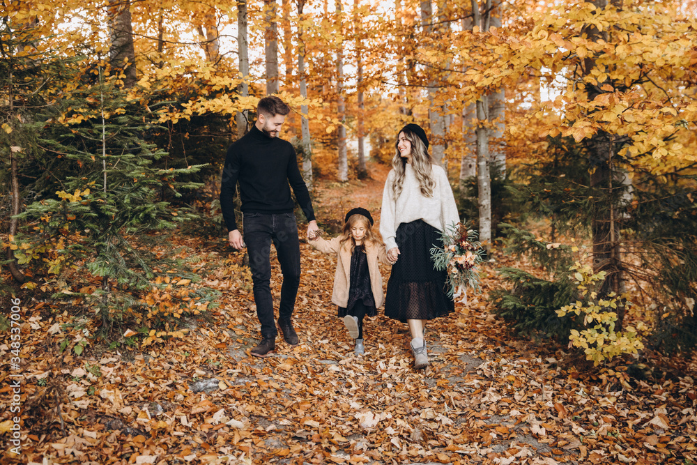 Stylish family in the autumn forest. A young guy and a girl are walking along a forest road among yellow leaves with their daughter. Stylish family in the autumn forest. A young guy and a girl are walking along a forest road among yellow leaves with their daughter.