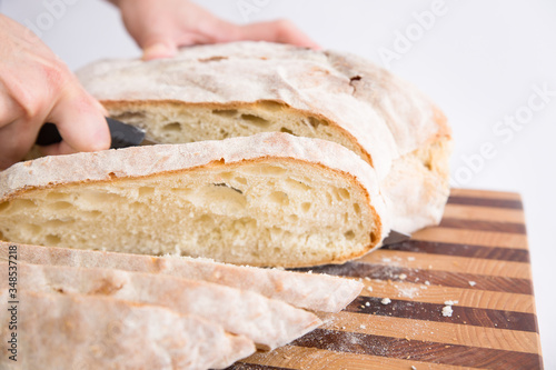 Closeup of fresh bread slices. Human hands cutting homemade loaf on chopping board. Isolated object on white background. Baking at home concept