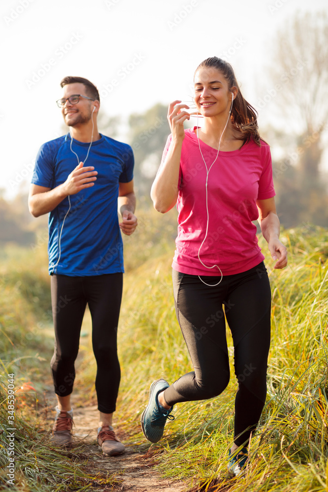 Happy young Caucasian couple jogging along footpath over a meadow in early morning on a beautiful summer day
