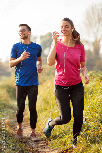 Obraz na płótnie Happy young Caucasian couple jogging along footpath over a meadow in early morning on a beautiful summer day w salonie