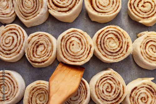 cooking home cinnabon buns from yeast dough on in row baking paper lie in a row and wooden spatula close up
