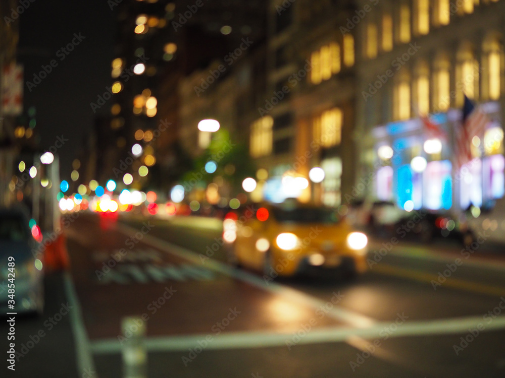 Defocus blur of New York City street scene at night with yellow taxi cabs, cars, lights and buildings.