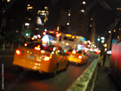 Defocus blur of New York City street scene at night with yellow taxi cabs, cars, lights and buildings.