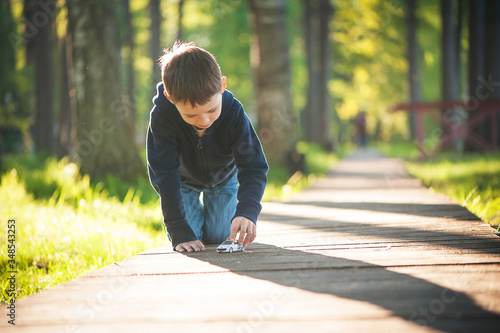 A boy plays a toy car on the street, rolls it along a wooden path, a lot of light and sun.