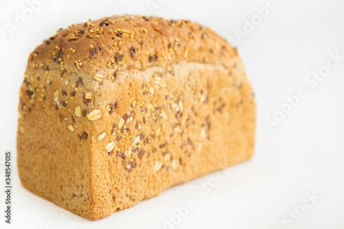 Homemade tasty brick form bread. Crusty whole loaf with cereals, oats, seeds isolated on white background. Studio shot. Selective focus. Side view. Home culinary and baking concept