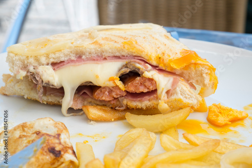 a francesinha cut in half, on a plate with fries. This sandwich originates in Porto, Portugal and is often served with a sauce 