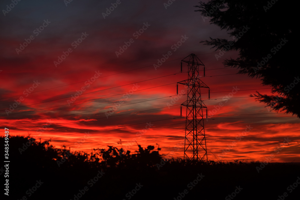 Naklejka premium An electricity pylon, also said transmission tower, stands in the countryside of Somerset, England. The sky is on fire right after sunset.