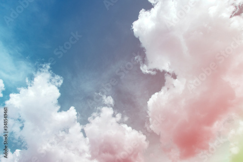 Colorful puffy fluffy cumulus clouds with gradient pink, purple & yellow colored on beautiful sunny blue sky in tropical summer or spring sunlight & sun rays, abstract surreal nature background 