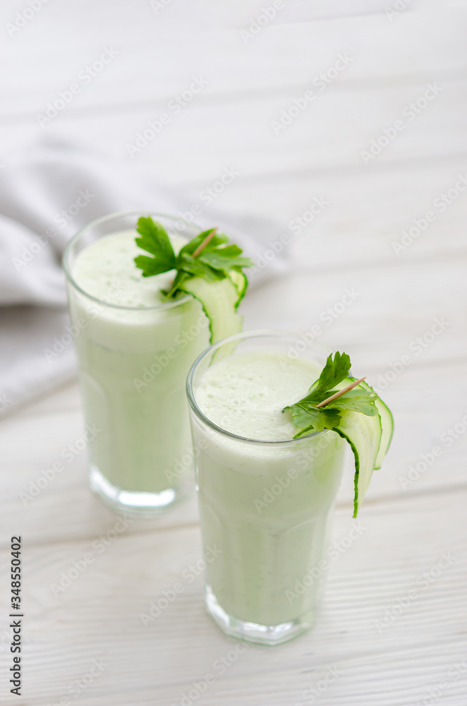 Refreshing fermented milk drink with cucumber and herbs. Two with such a cocktail in a light interior on a white table. Refreshing fermented milk drink with cucumber and herbs. Two with such a cocktail in a light interior on a white table.