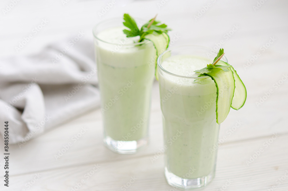 Refreshing fermented milk drink with cucumber and herbs. Two with such a cocktail in a light interior on a white table. Refreshing fermented milk drink with cucumber and herbs. Two with such a cocktail in a light interior on a white table.