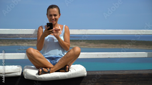 Woman using cellphone texting sms message outside on balcony terrace of luxury hotel by the sea
