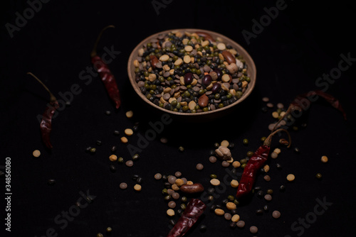 A bowl of Indian mixed pulses decorated with cereals and dried chilli in a dark copy space background. Food and product photography.