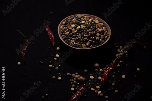 A bowl of Indian mixed pulses decorated with cereals and dried chilli in a dark copy space background. Food and product photography.