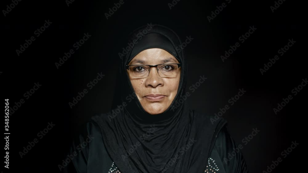 Close up of a muslim woman in hijab on black background. Arabic woman wearing eyeglasses staring at camera.
Close up of a muslim woman in hijab on black background. Arabic woman wearing eyeglasses staring at camera.