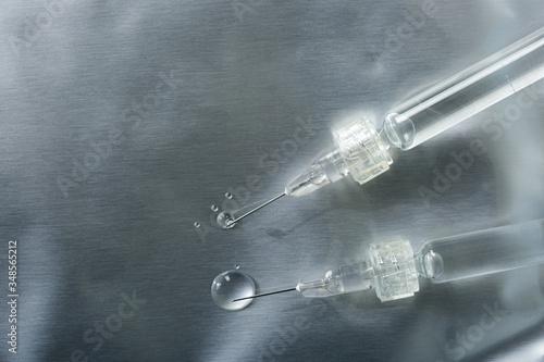 close-up of two syringes with a Luer lock with needles and drops of injections leaking on a silver background and copy space on the left photo