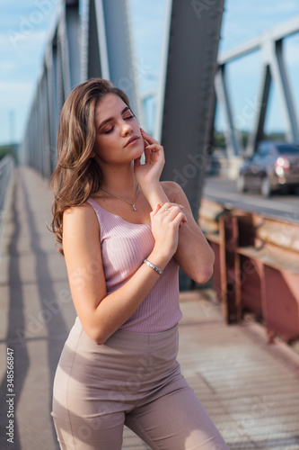 Pretty young woman posing on the old rusty transport bridge over the river during sunset.