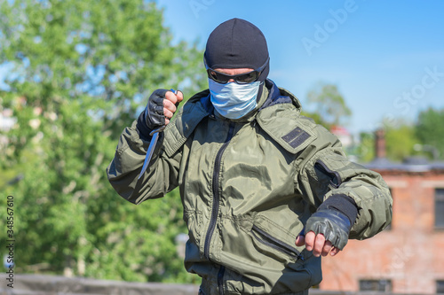A thug in a medical mask and black glasses with a knife in his hands attacks people passing by © Николай Чекалин