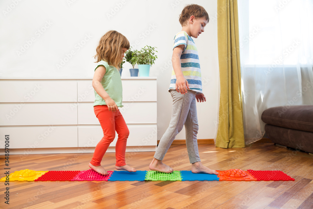 Two kids of presschool children walk on an massaging mat at home