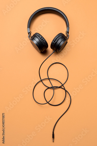 Photo of stylish modern black headphones over beige background.