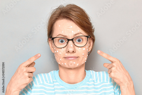 Portrait of cute puzzled girl with white drops of face cream on skin